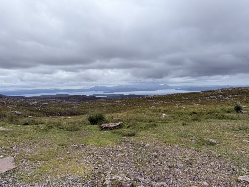 Applecross Pass view of hills, water, and mountains beneath heavy cloud.