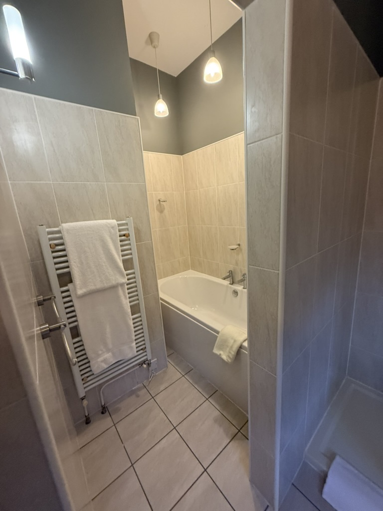 Modern bathroom with beige tiles, white bathtub, and pendant lights.