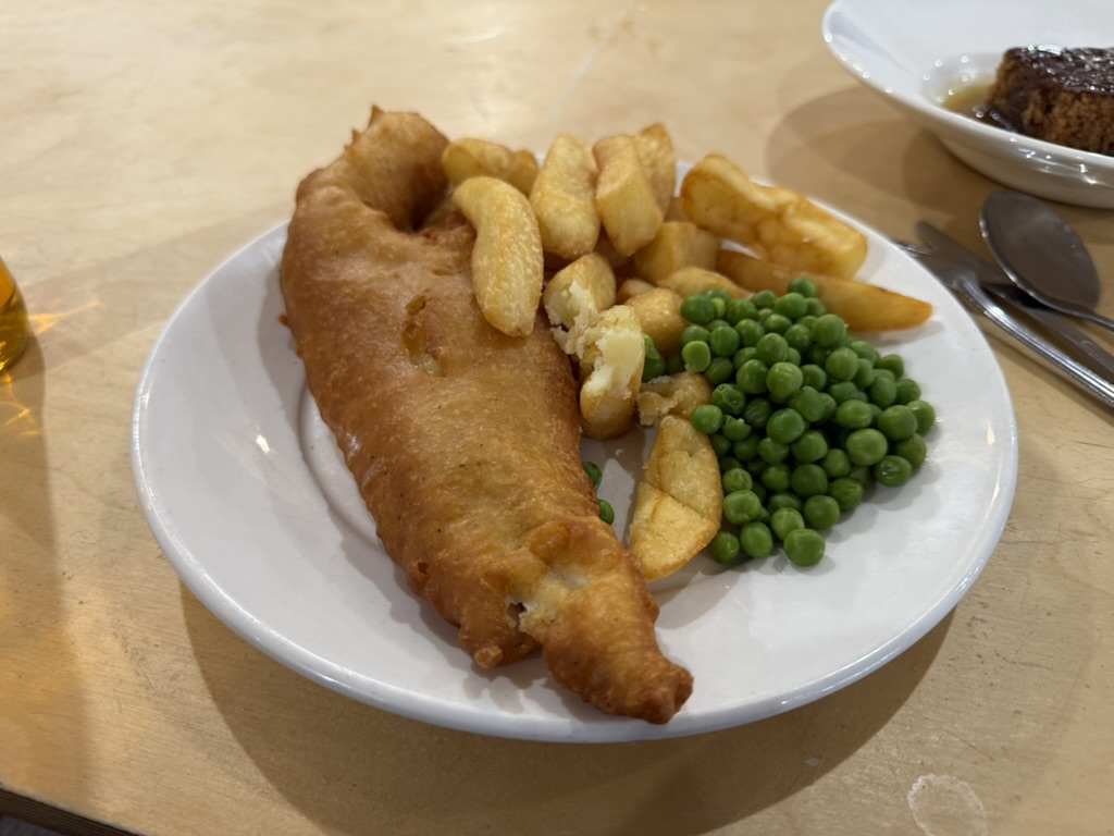 Plate of fish and chips with peas on a wooden table.