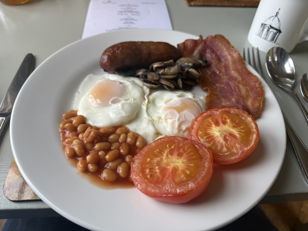 Plate with English breakfast of eggs, beans, bacon, sausage, mushrooms, and tomato.