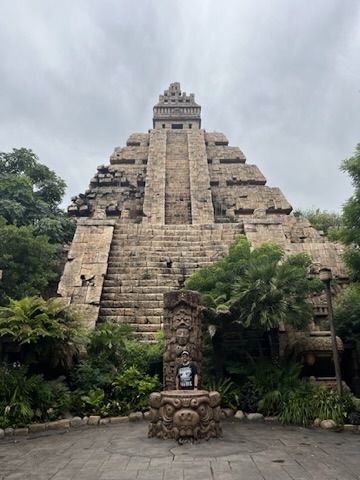Matthew Jones standing in front of a large ancient American temple structure surrounded by greenery, which is the entrance to the Indiana Jones ride
