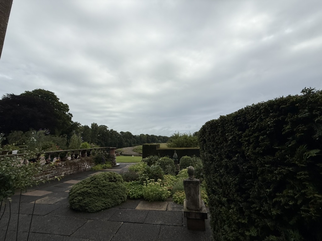 Formal garden at Warrick Hall with hedges, statues, and a paved walkway.