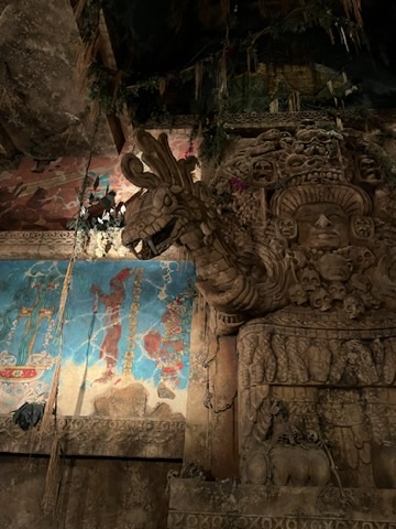 A carved stone wall featuring a dragon-like creature and intricate ancient designs, with faded murals in the background. This in in the Indian Jones ride