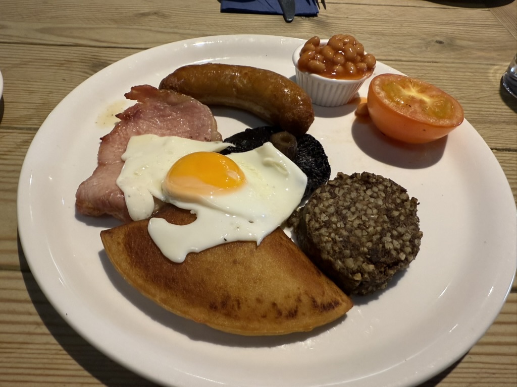 Scottish breakfast plate with egg, bacon, sausage, black pudding, beans, potato scone, tomato, and haggis