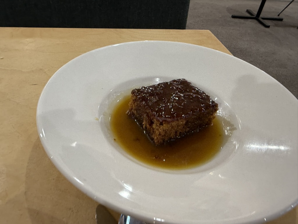 Sticky toffee pudding topped with warm toffee sauce on a white plate.