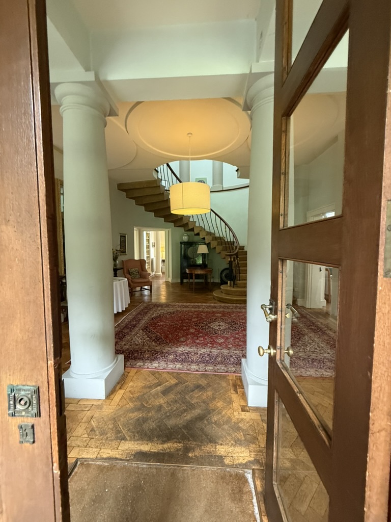 Elegant foyer with columns, red rug, and curved staircase.