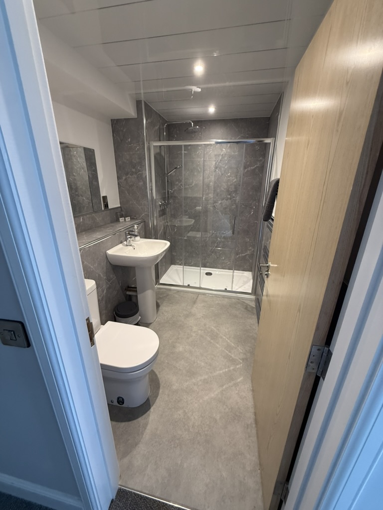 Modern bathroom with glass shower, pedestal sink, and grey tiled walls.