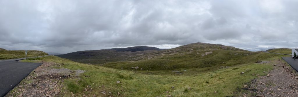 Applecross Pass view with winding road, camper van, and cloudy highland scenery.