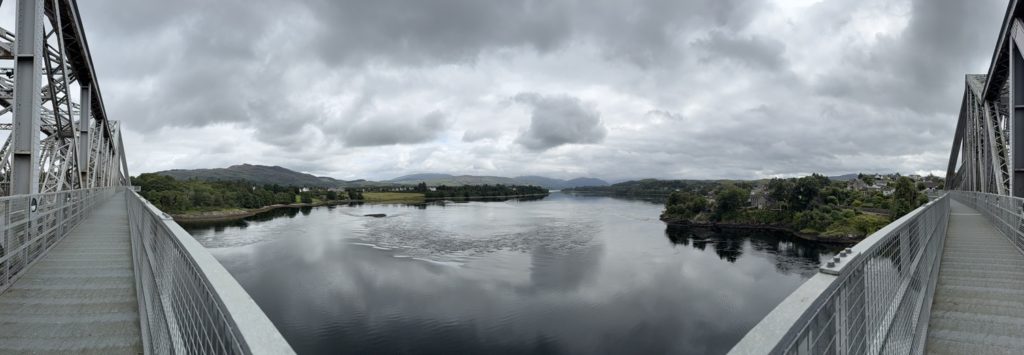 View from Connel Bridge overlooking wide river, hills, and village under cloudy sky.