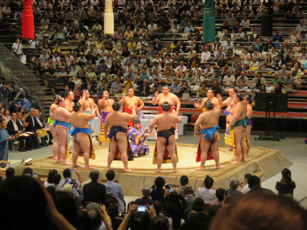 Sumo wrestlers gathered in a ring during a ceremonial event in a crowded arena.