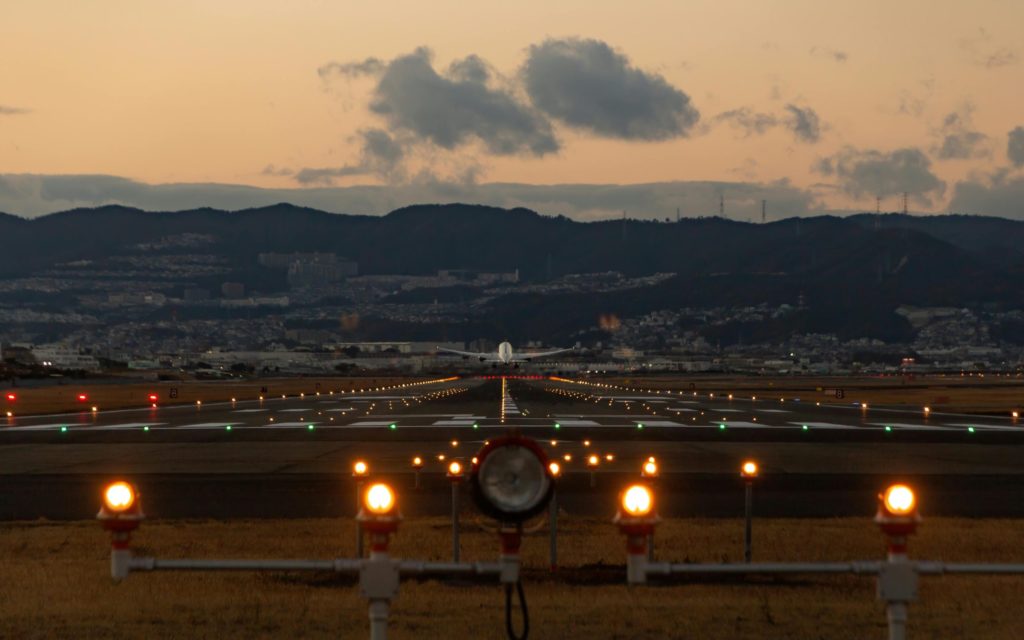Airplane taking off from a lit runway at dusk with mountains in the background.